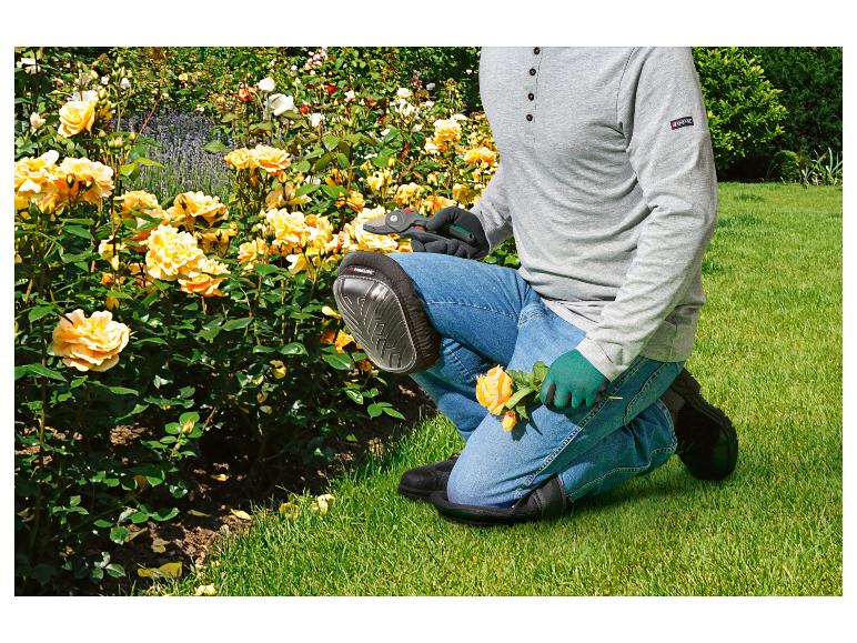 Záhradník kľačiaci, s chráničmi kolien a rukavicami, strihá žlté ruže.