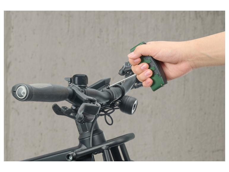 Ruka držiaca zelený nástroj na riadidlách bicykla s príslušenstvom.