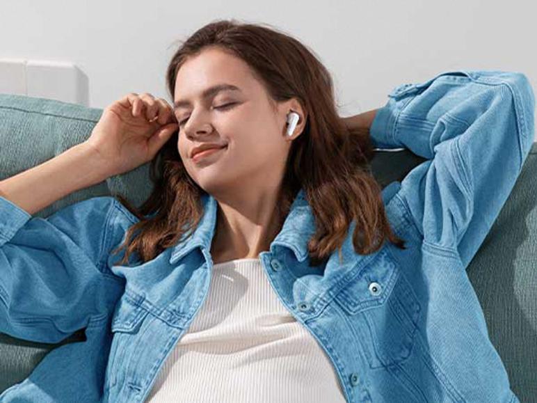 Žena relaxuje na pohovke a počúva hudbu s bielymi slúchadlami do uší.