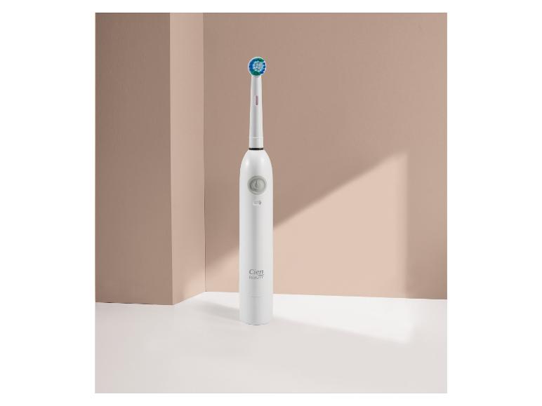 Biela elektrická zubná kefka Cien Beauty so zelenou a modrou hlavicou na béžovom pozadí