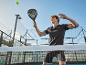 Muž hrajúci padel s raketou, loptou a kurtom v pozadí.