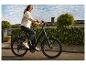Mladá žena v džínsovej bunde a tmavých džínsoch jazdí na e-bicykli po obytnej ulici.