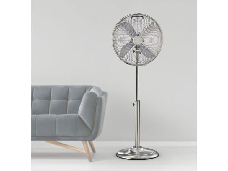 Strieborný stojací ventilátor v miestnosti s šedou pohovkou.