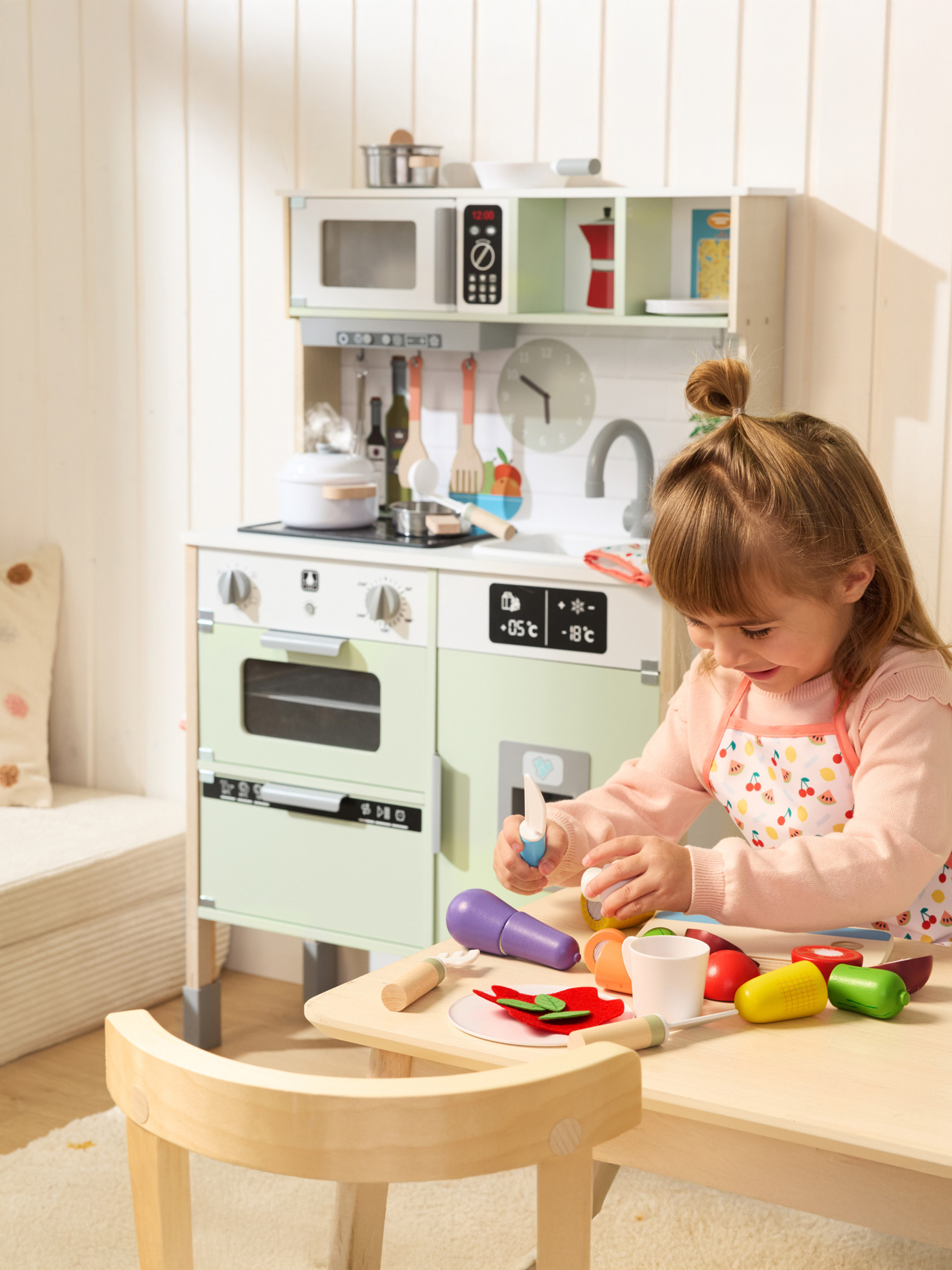 Dievča sa hrá s drevenou hračkárskou kuchynkou a príslušenstvom na varenie.