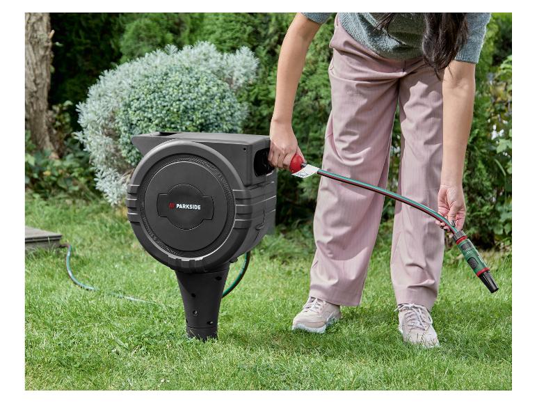 Žena vyťahuje záhradnú hadicu z automatického navijaka v zelenej záhrade.
