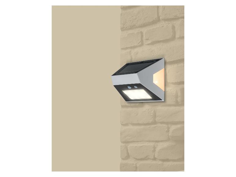 Solárna nástenná lampa s pohybovým senzorom a dvoma svetlami, namontovaná na tehlovej stene.