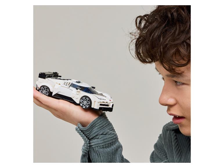 Mladý muž sa pozerá na biele miniatúrne pretekárske auto, ktoré drží v ruke.