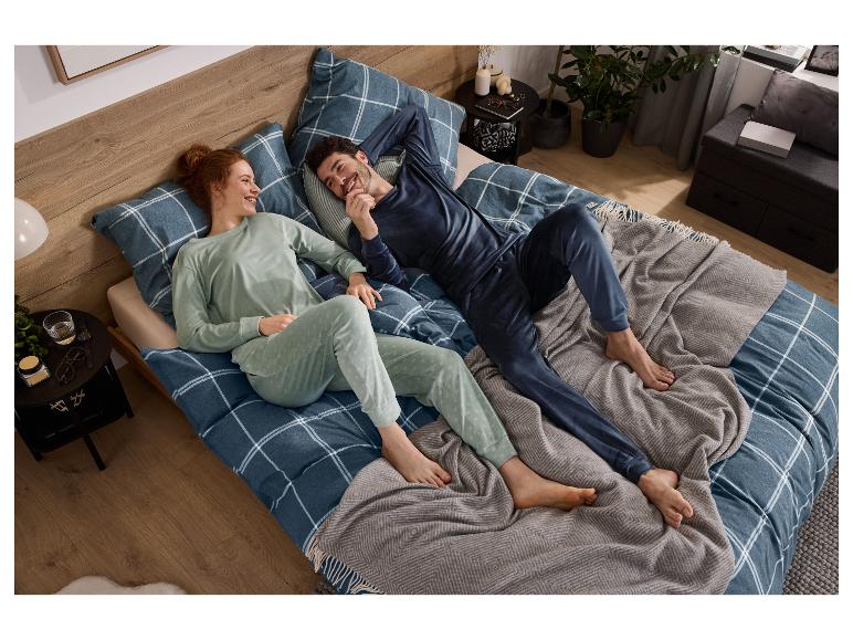 Usmiaty pár relaxuje v posteli, oblečený v zladených pyžamách, s károvanou posteľnou bielizňou.