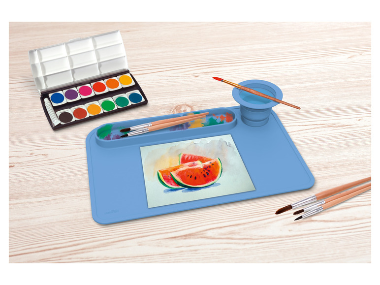 Sada vodových farieb, štetce a modrá silikónová podložka na maľovanie.