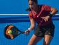 Žena hrajúca padel s raketou a loptičkou na modrom kurte.