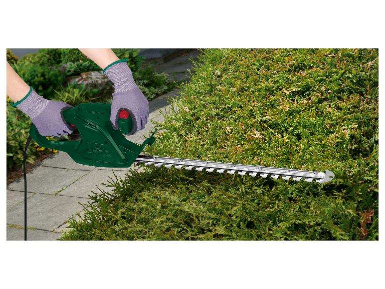 Osoba používa zelený elektrický strihač živého plota značky Scheppach na strihanie živého plota.