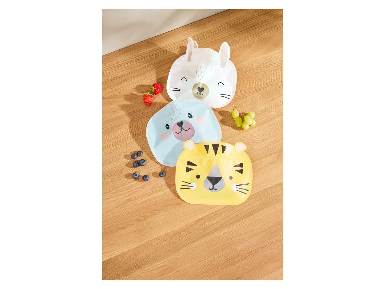 Tri opakovane použiteľné vrecká v tvare zvierat, naplnené ovocím, na drevenom pozadí.