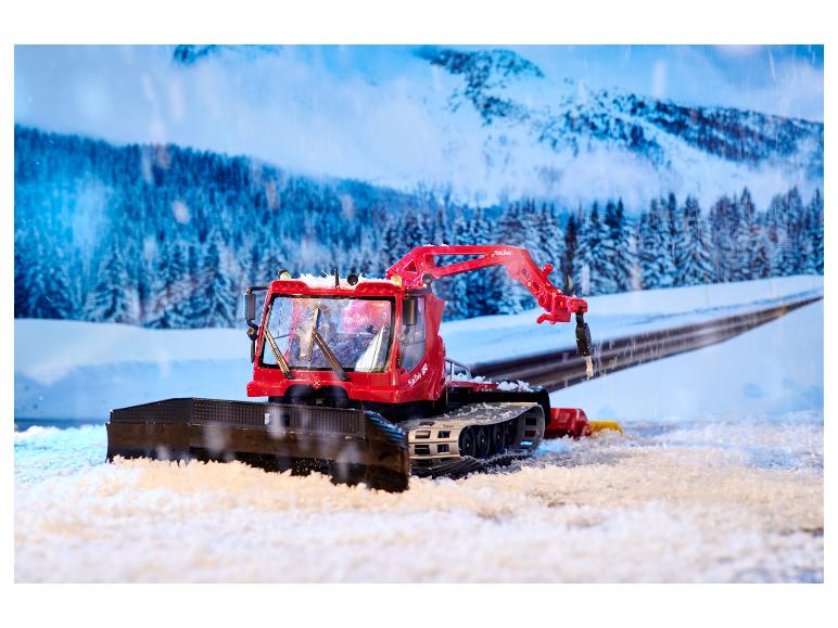 Červený snežný skúter PistenBully 600 so snežným pluhom v zimnej krajine.