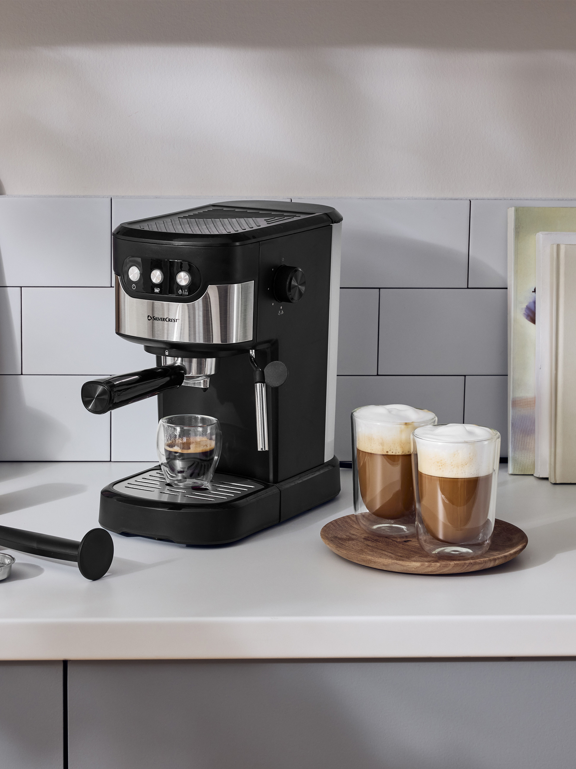 Čierny kávovar na espresso na bielej kuchynskej linke s dvoma šálkami kávy.
