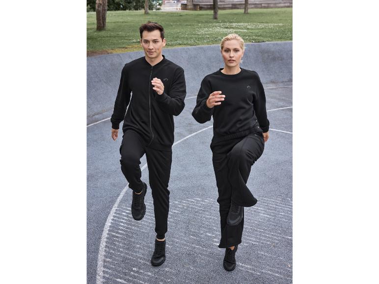Muž a žena v čiernych teplákoch a teniskách Reebok, cvičia vonku.
