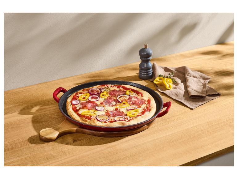 Pizza so salámou, červenou cibuľou a paprikou v liatinovej panvici na drevenom stole.