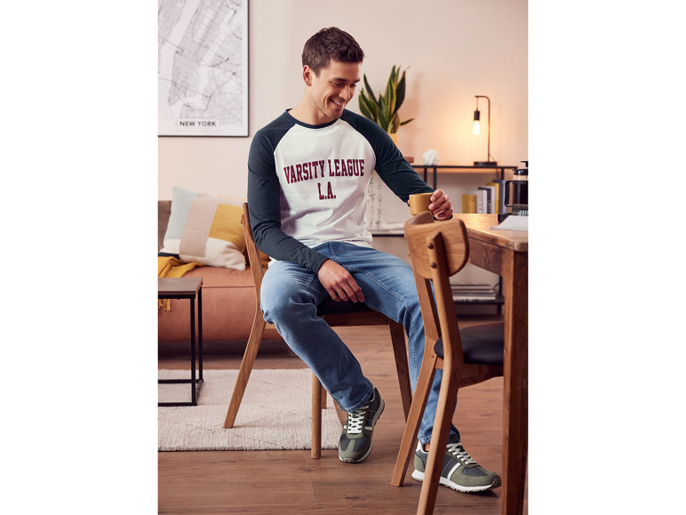 Muž v bielom tričku s modrými džínsami a zelenými teniskami.