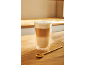 Latte macchiato v sklenenej šálke a zlatá lyžička na drevenom stole.