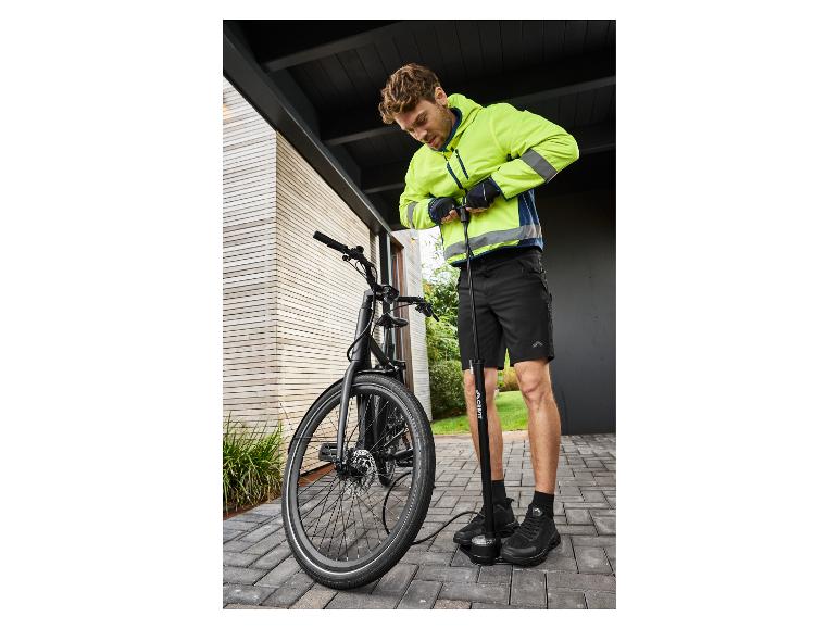 Muž v neónovo žltej bunde a čiernych šortkách pumpuje pneumatiku bicykla podlahovou pumpou.
