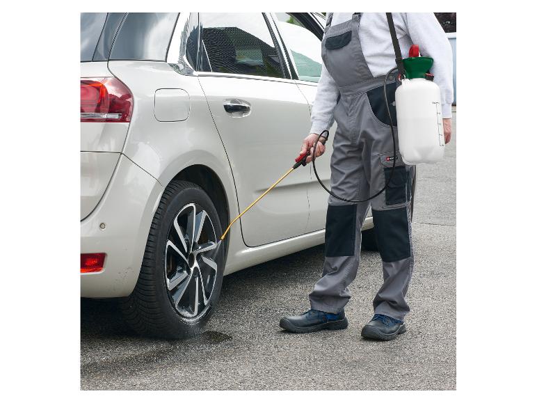 Muž v montérkach čistí pneumatiky auta pomocou tlakového postrekovača.