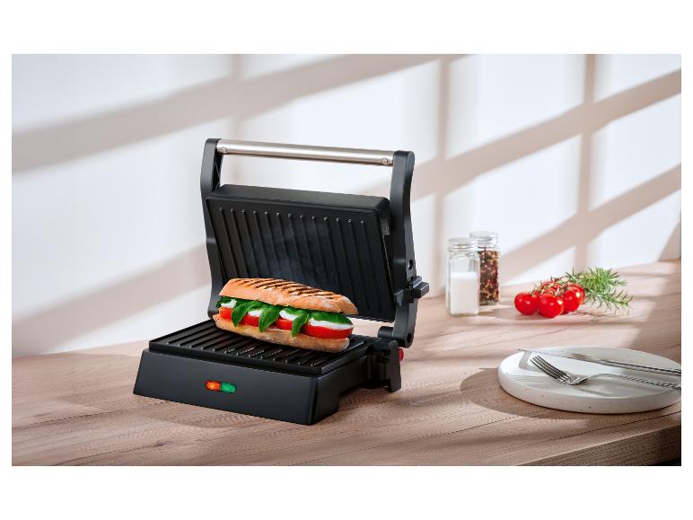 Otvorený panini gril s Caprese sendvičom na drevenej doske.