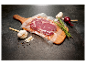 Vakuumové balený hovädzí steak na drevenej doske s cesnakom, cibuľou a rozmarínom.