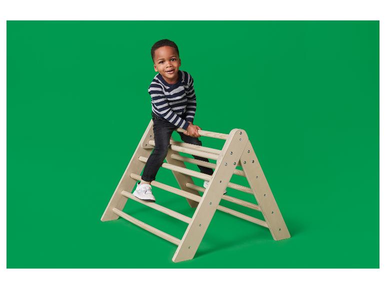 Šťastný chlapec lezie na drevenú trojuholníkovú preliezačku.