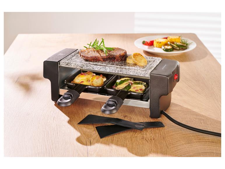 Raclette gril so steakom, zemiakmi a cuketou na drevenom stole.