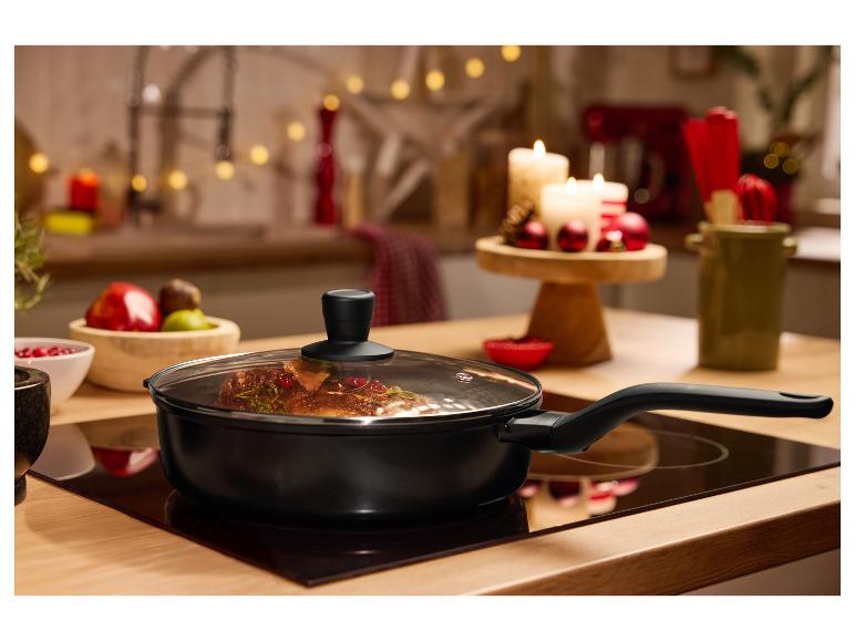 Čierna panvica so sklenenou pokrievkou na varnej doske, s vianočnou výzdobou v pozadí.