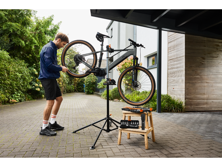 Muž opravuje elektrický horský bicykel na opravnom stojane s náradím vedľa.