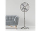 Strieborný stojací ventilátor v miestnosti s šedou pohovkou.