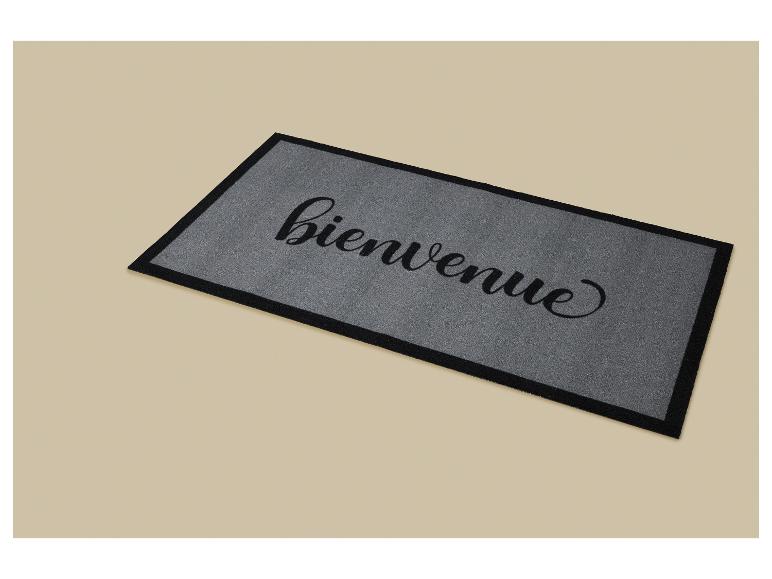 Sivá rohožka s nápisom „bienvenue“ (vitajte) čiernym kurzívnym písmom.