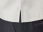 Detail béžovej košele so štrbinami, nosenej s čiernymi nohavicami.