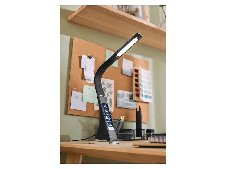 Čierna LED stolná lampa s digitálnym displejom na drevenom stole s korkovou tabuľou.