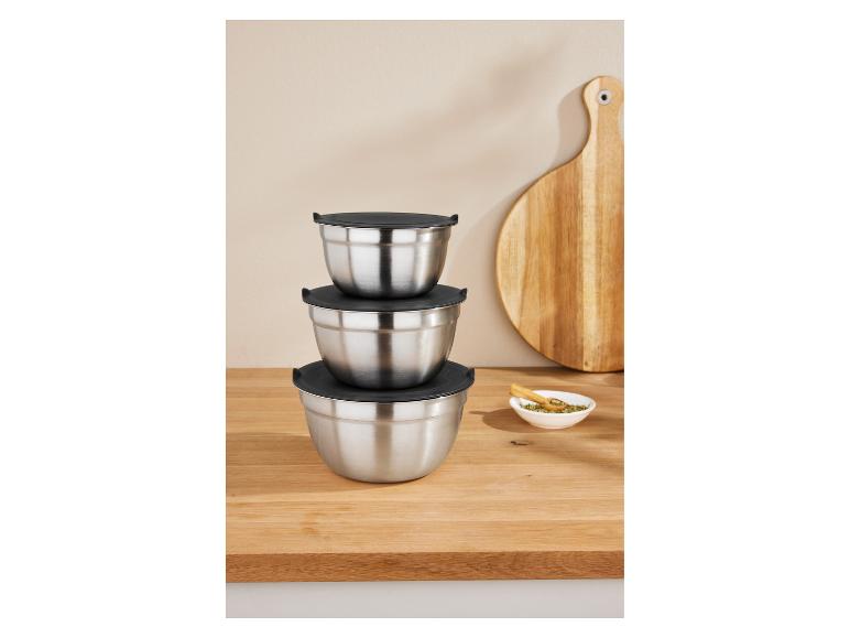 Tri naskladané nerezové misky na miešanie s čiernymi viečkami na drevenom stole.