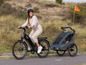 Žena ide na bicykli s elektrickým pohonom s detskou priestrannou Qeridoo za sebou.