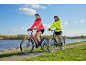 Muž a žena jazdia na bicykloch po dláždenej ceste pri vode.
