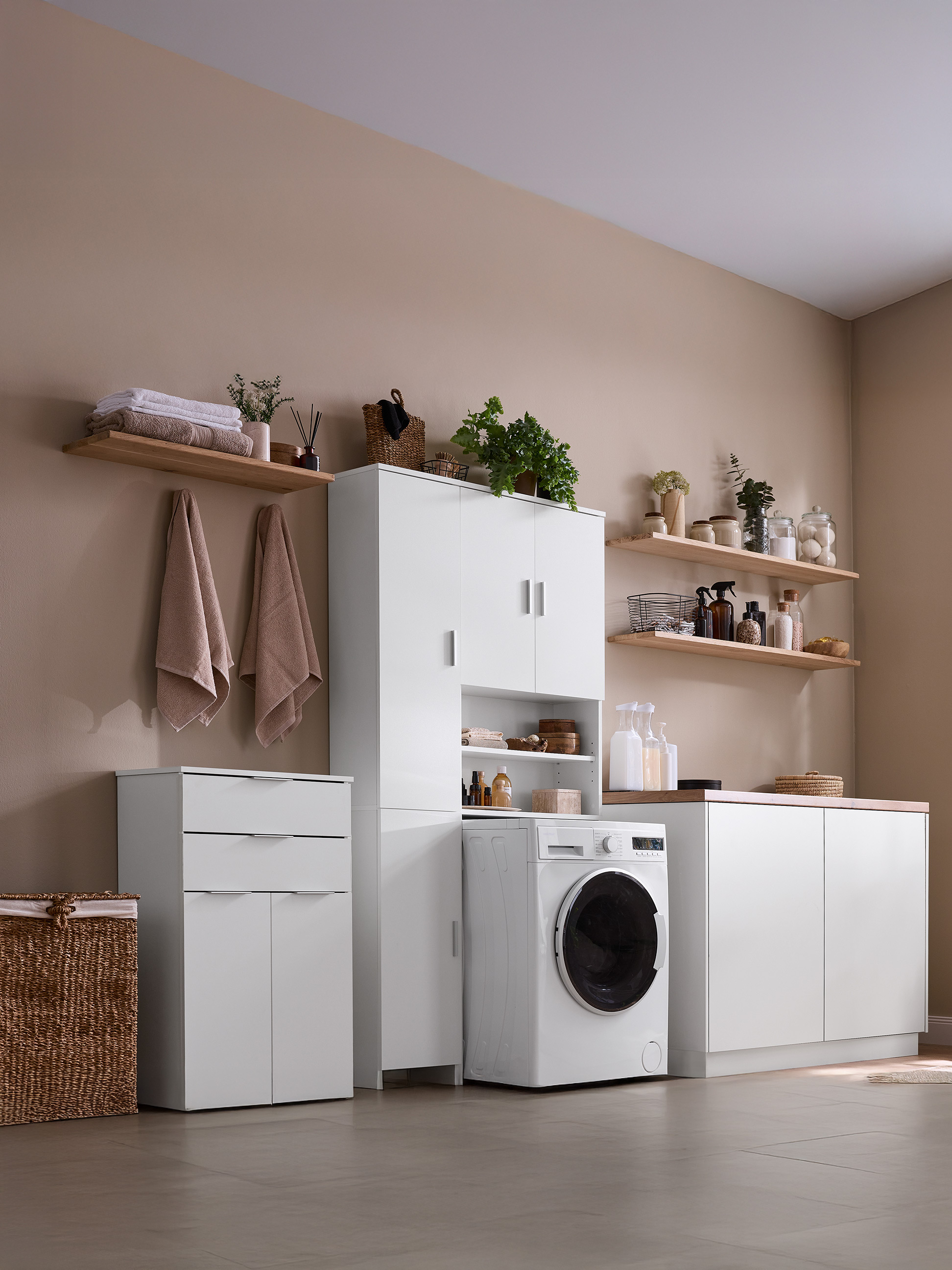 Moderná práčovňa s bielymi skrinkami, policami, práčkou a prúteným košom.