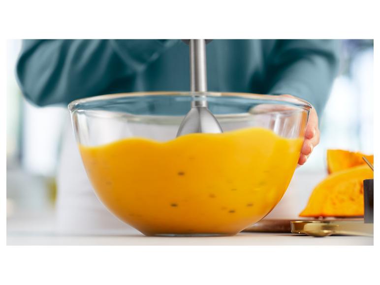 Osoba mixuje tekvicovú krémovú polievku v sklenenej miske ponorným mixérom.