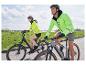 Dve osoby idú na bicykloch v jasnožltých vestách.