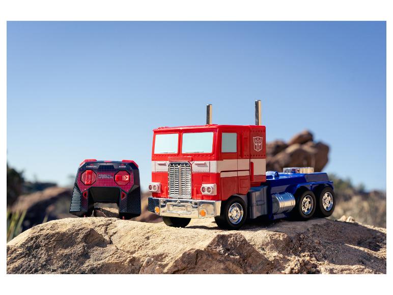 Hračka kamión Optimus Prime a diaľkové ovládanie na skalnatom teréne pod jasnou oblohou.