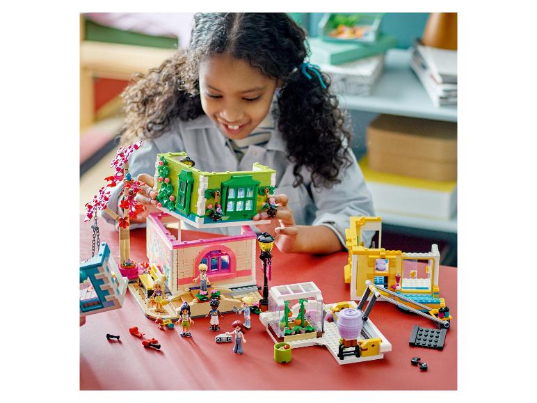 Usmiate dievča skladá domček pre bábiky LEGO Friends, s ďalšími súpravami okolo.