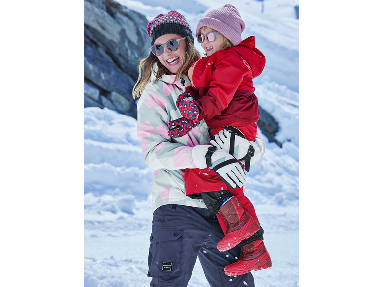 Žena a dieťa v zimnom oblečení, vrátane červenej bundy a 'Mountain Slopes' nohavíc.