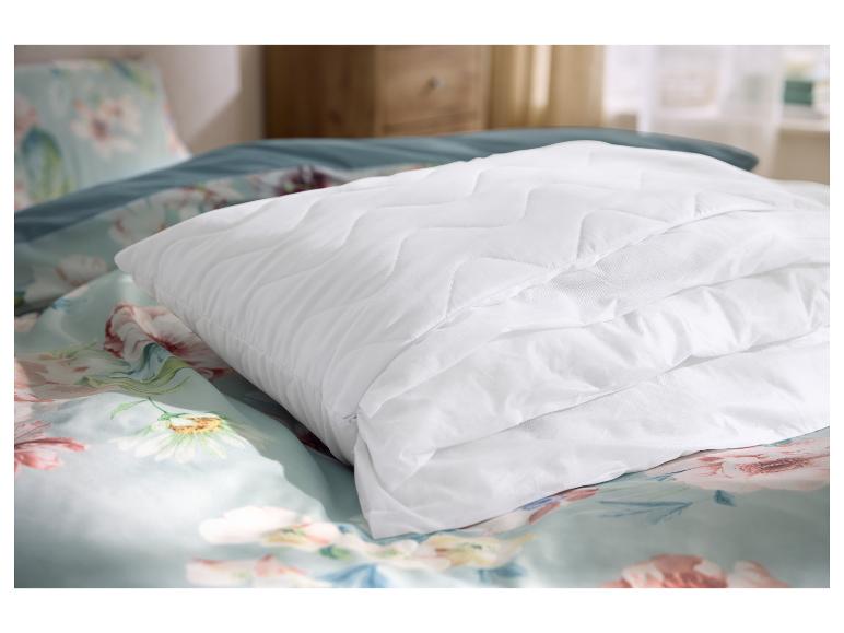 Prešívaný biely chránič matraca na kvetinovej posteľnej bielizni v spálni.