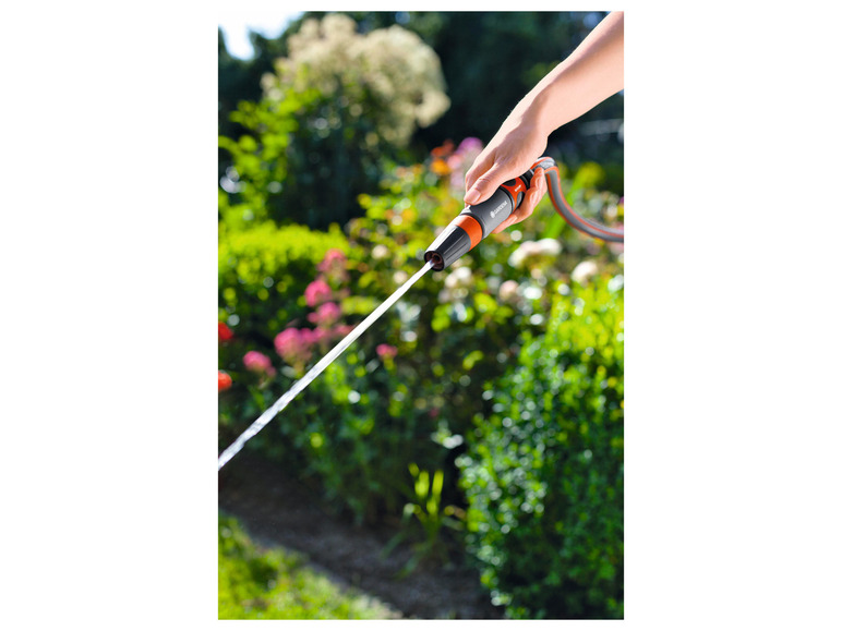Ruka drží záhradnú hadicu Gardena a strieka vodu na zelenú záhradu.