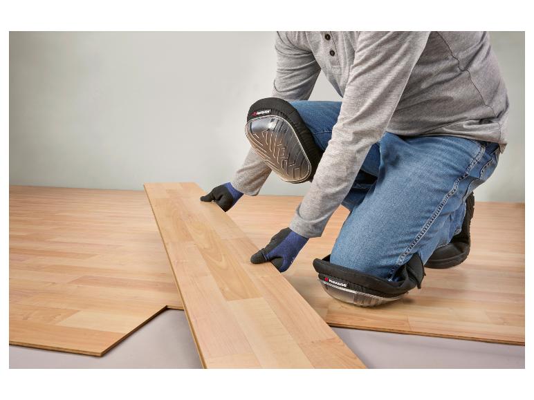 Muž inštaluje laminátovú podlahu, má na sebe chrániče kolien a rukavice.