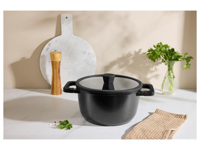 Čierny hrniec s pokrievkou, mlynček na korenie, doska na krájanie a petržlen v kuchyni.