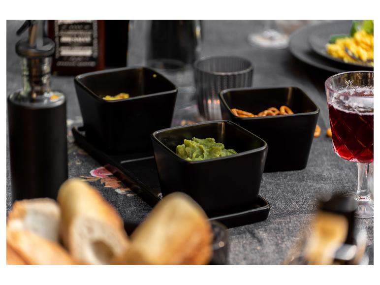 Čierne misky s guacamole, pretzelmi a bagetou na stole.