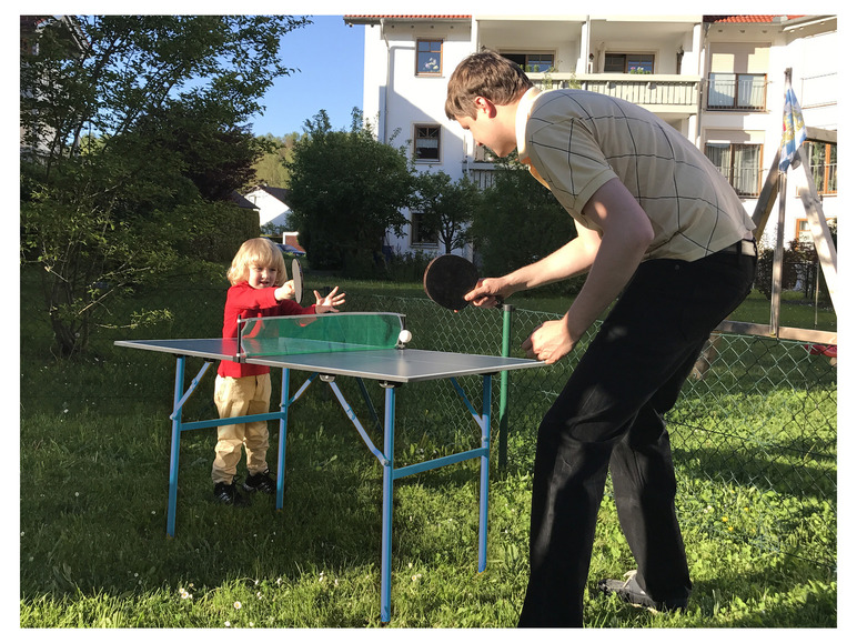 Dospelý a dieťa hrajú stolný tenis v záhrade.