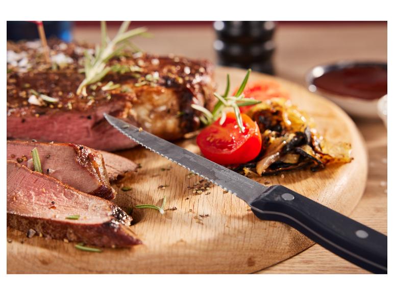 Grilovaný steak s nakrájanou cibuľou a paradajkami na drevenej doske s nožom.